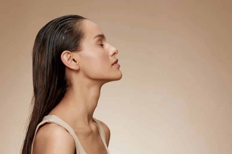 Profile portrait of a serene woman with long, wet hair against a neutral background, showcasing natural beauty and calm emotions in a minimalistic style