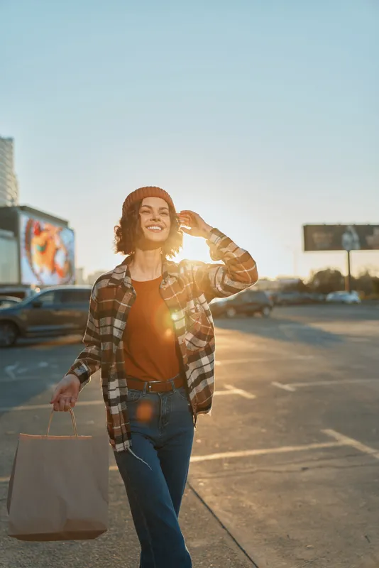 Woman smile shopping in urban parking lot at sunset, candid lifestyle portrait capturing authenticity and golden hour glow, mindful living vibe with emotional storytelling.