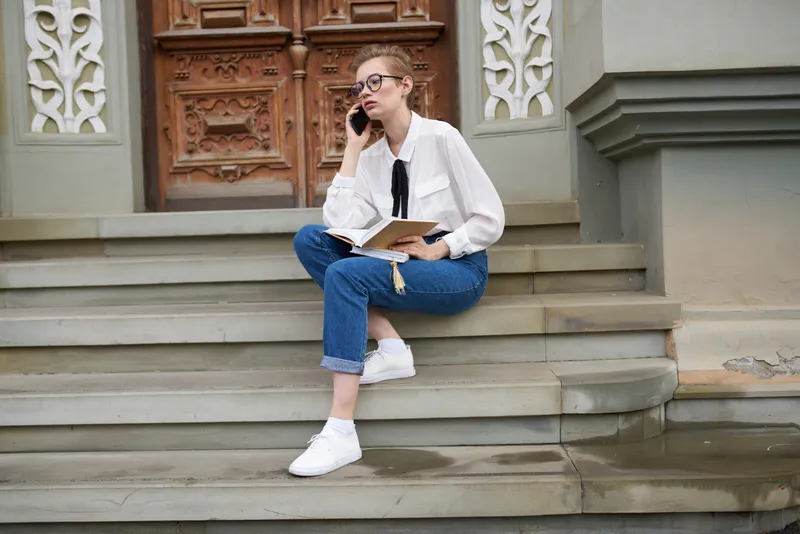 Студентка с книгой на ступенях у здания учебного заведения, в очках