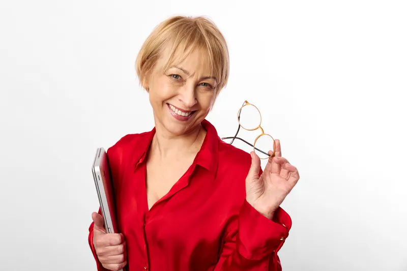 Smiling woman holding eyeglasses in a white studio portrait. Close up focus, confident expression, concept of vision care, eyewear, technology, and daily life.