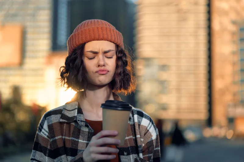 Woman coffee beanie expression urban morning cup portrait experiencing authenticity and candid lifestyle with golden hour glow, mindful living and emotional storytelling in a city street scene.