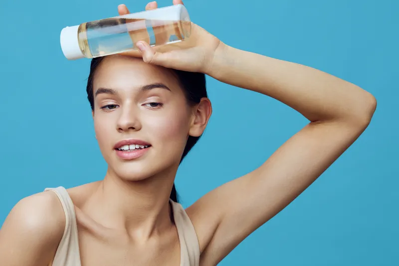 Young woman with a skincare product on her forehead, exhibiting a playful smile against a light blue background, embodying beauty and self care concepts