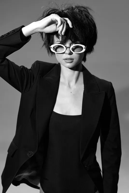 Stylish woman with sunglasses wearing a black jacket in a black and white portrait.