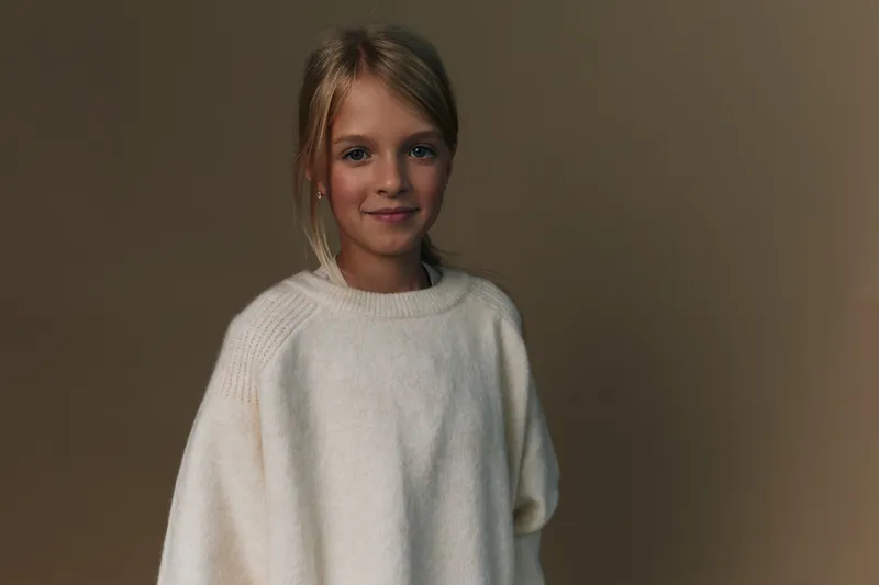 Authentic portrayal of a young girl in a cozy knit sweater, capturing a simple, candid moment ideal for lifestyle and school themed projects.