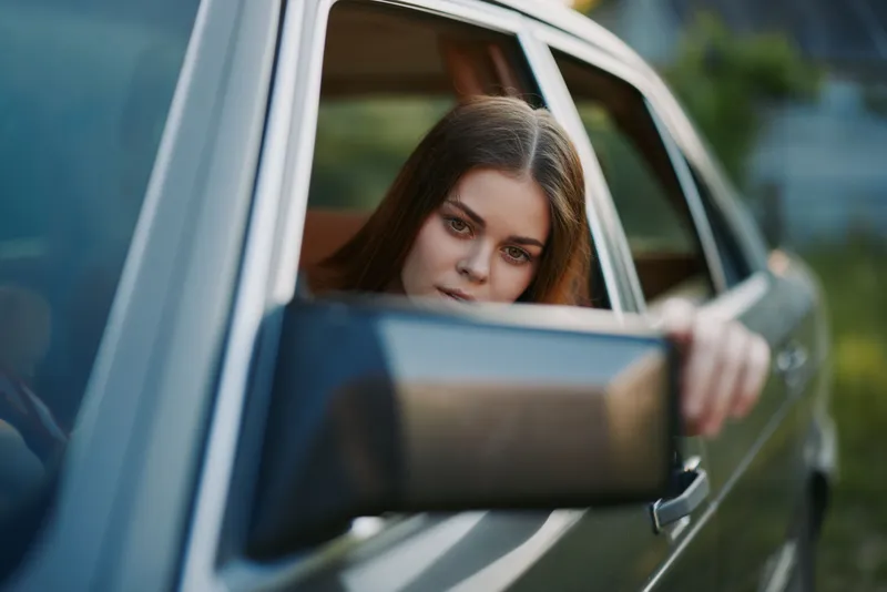 Young woman reflecting on life while leaning out of a car window, showcasing emotions and a serene outdoor background. KEY: woman, car, reflection, outdoor, emotions, serenity, lifestyle, thoughtful,