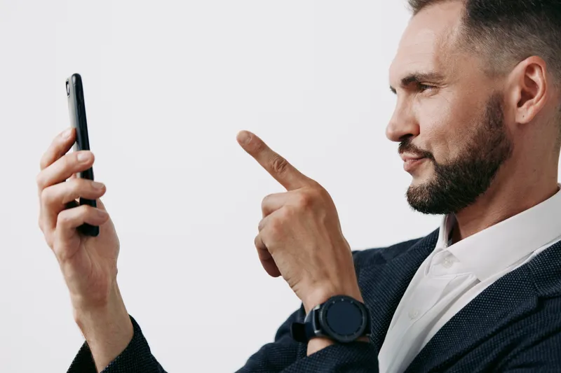 Professional man in business attire checks a smartphone, eyes focused and expression confident, posed against a colored backdrop to convey modern work life and clear communication.
