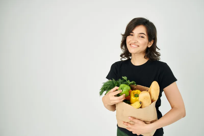 Весёлая брюнетка в чёрной футболке с пакетом продуктов из супермаркета