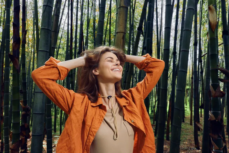 Woman bamboo forest outdoor happy nature smile relaxed portrait, woman with hands in hair and eyes closed enjoying a serene bamboo grove, peaceful wellness and nature escape.