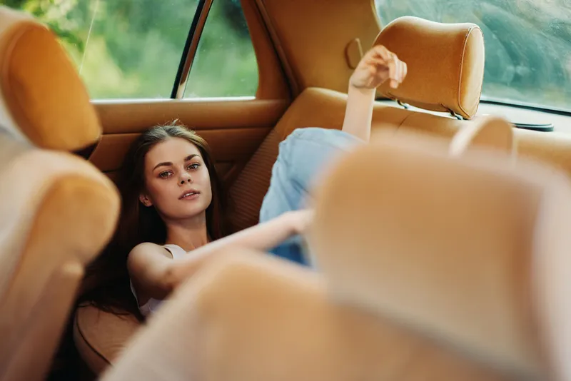 Young woman relaxing in a vintage car, wearing casual clothes, expressing tranquility while surrounded by warm earthy tones and soft natural light.
