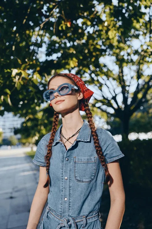 lifestyle woman in modern boho-western denim street style with blue sunglasses and red bandana, captured in natural light with vibrant film color tones, outdoors on sunny day