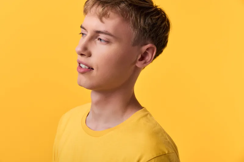 Young man in a yellow shirt stands against a bright yellow background with studio lighting, creating a casual style and warm mood ideal for lifestyle, fashion or wellness campaigns