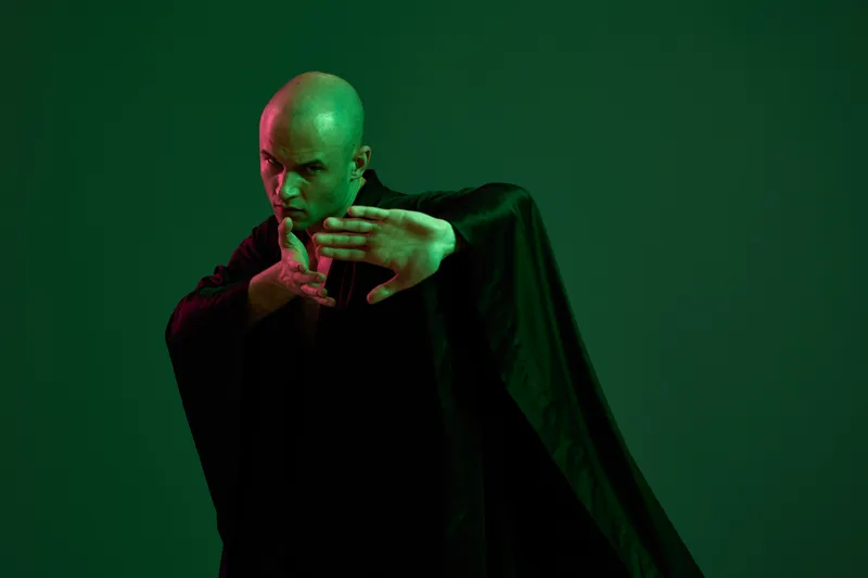 Mysterious man in a black cloak poses dramatically against a dark green backdrop, creating an aura of intrigue and power. Perfect for artistic projects or storytelling.