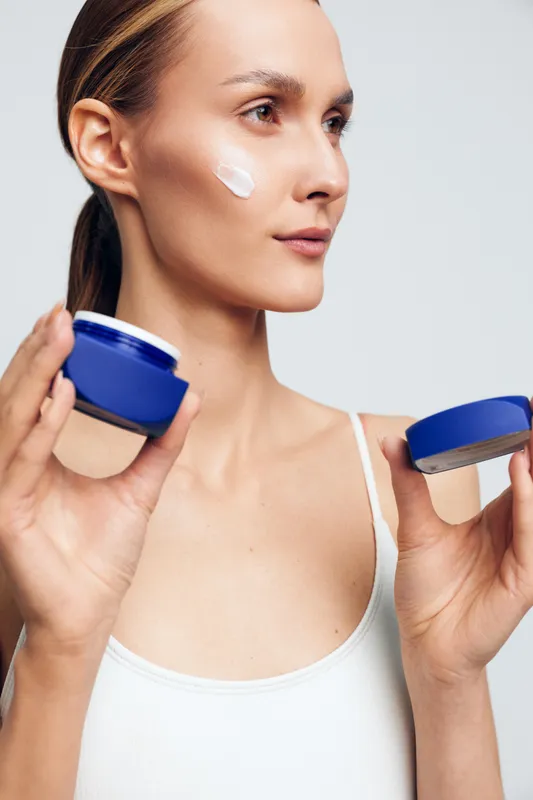 Woman applying face cream from blue jar, close up profile, studio lighting on white background, skincare and beauty self care, wellness concept, smooth skin today