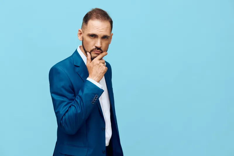 A professional man in a tailored blue suit stands against a solid blue backdrop, projecting calm focus and poised executive emotion, ready for insight and leadership.