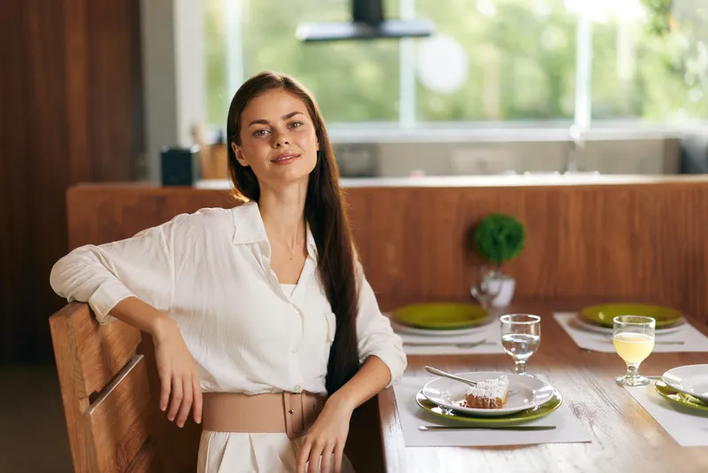Улыбающаяся женщина наслаждается романтическим ужином дома с вкусным домашним тортом и вином