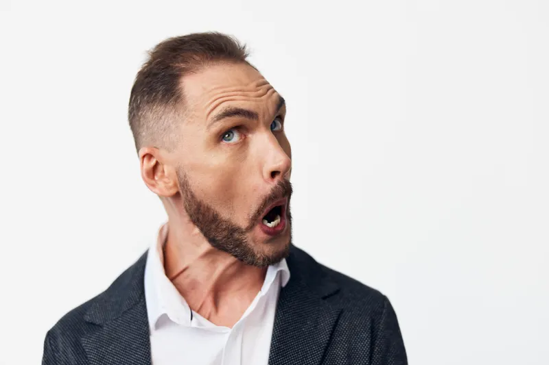A professional business man stands against an isolated colored background, showing a surprised and expressive emotion that conveys curiosity, alertness, and readiness in a modern corporate setting.