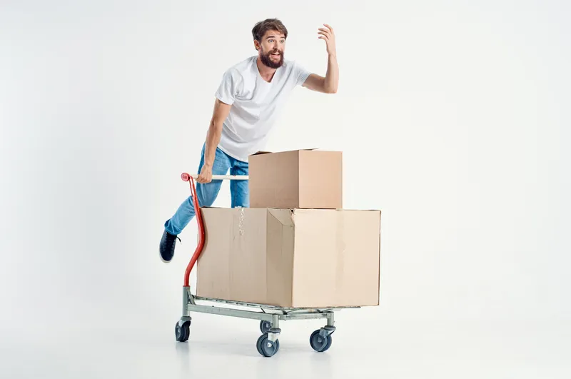 Весёлый мужчина занимается доставкой транспорта в коробке на светлом фоне