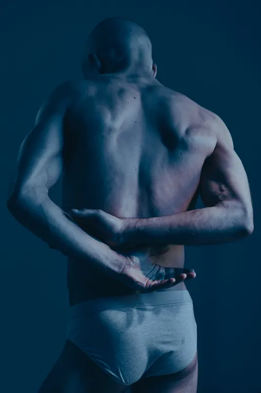 Athletic man with a strong physique posing dramatically in low lighting, showcasing powerful muscles and an intense expression. A captivating black and white image.