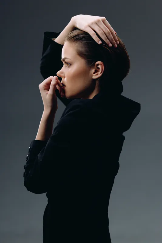 thoughtful woman in black clothing with hand on head looking sideways on dark background