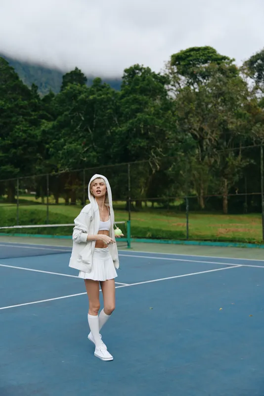 Young woman in sports attire on a tennis court, showcasing passion and energy in a serene outdoor setting with green trees and grey skies