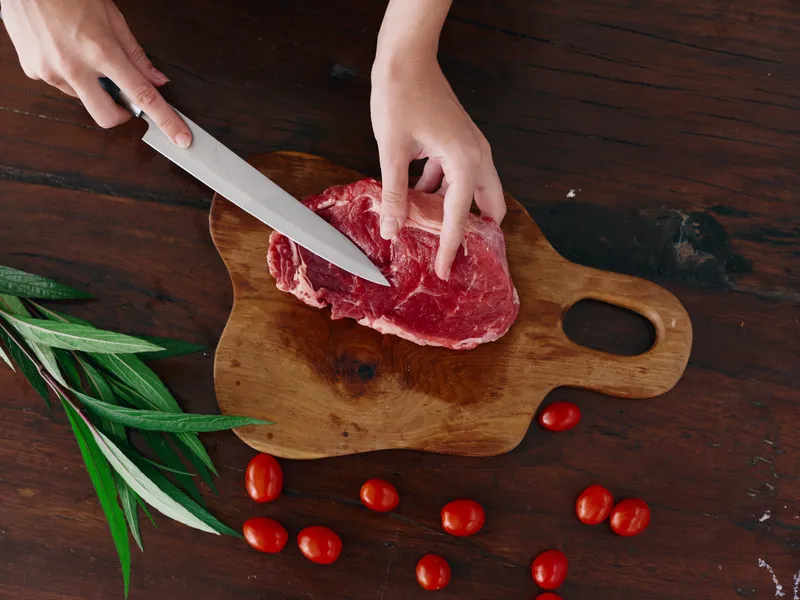 Женщина с ножом в руке нарезает свежее мясо стейка для жарки на кухне