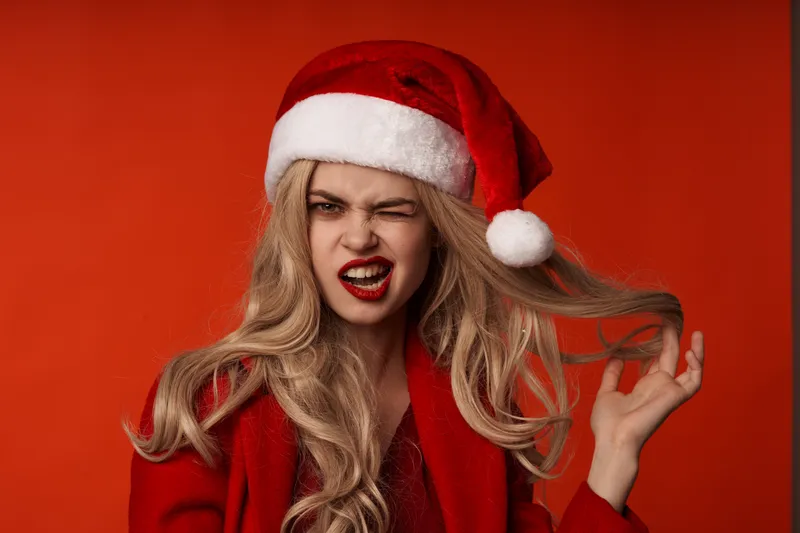 Женщина в рождественской одежде весело позирует на красном фоне во время праздника