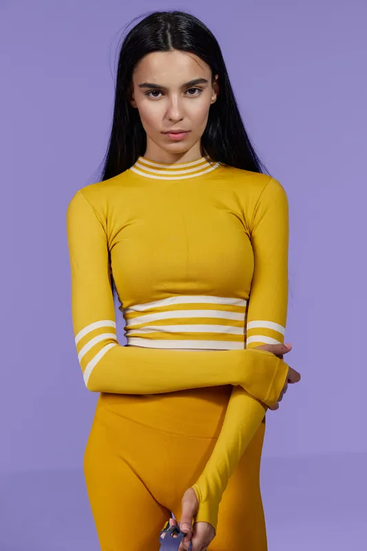 Woman sport fitness in yellow activewear, long sleeve top and matching leggings, standing confidently against purple background, stylish and modern athletic look.