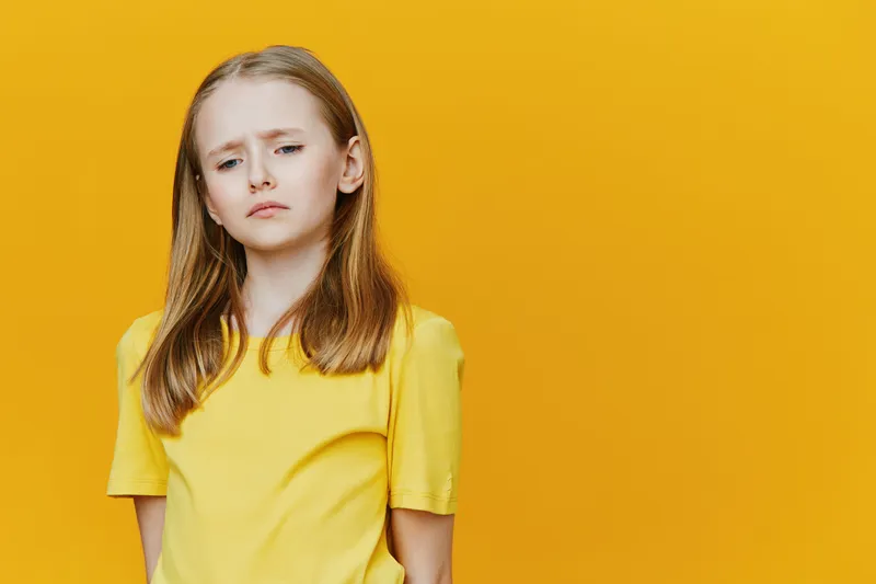 Sad little girl in a yellow t shirt against a vibrant yellow background, expressing feelings of disappointment and sadness, perfect for exploring childhood emotions