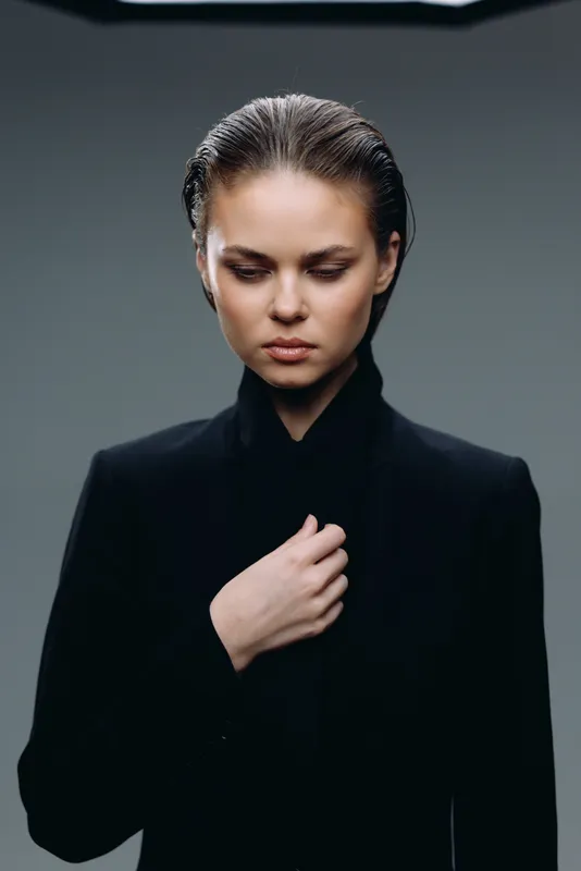 Serious woman in black suit with sleek hair looking down in moody studio lighting