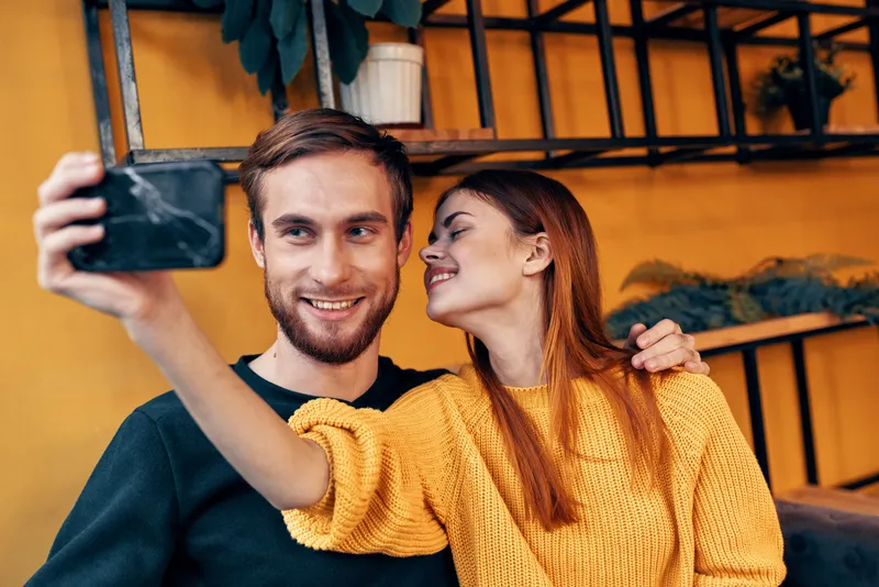 Женщина с мобильным телефоном и счастливый мужчина, друзья, веселье, семейное общение в интерьере