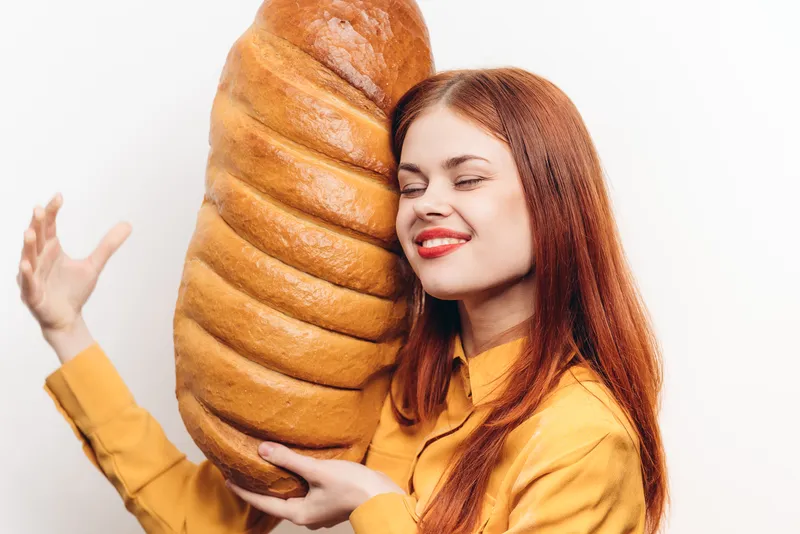 Счастливая женщина обнимает буханку хлеба, мучной продукт, светлый фон, обрезанный вид