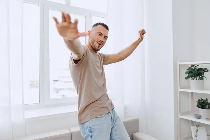 Dynamic man joyfully dancing indoors, showcasing a modern lifestyle with a bright background, embracing the essence of happiness and movement.