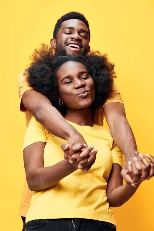 Joyful couple with Afro hairstyles wearing matching yellow shirts against a bright yellow background, showcasing love and happiness