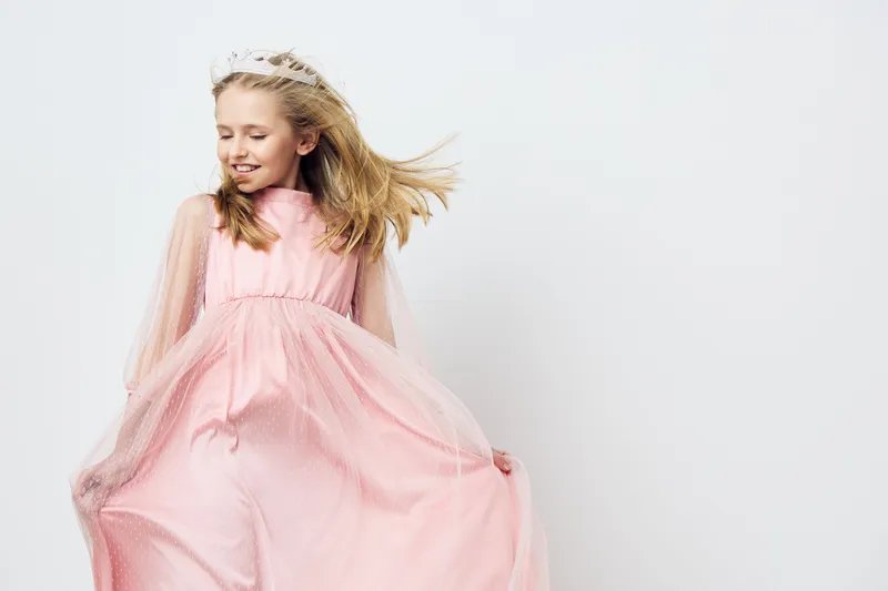 Joyful girl in a pink dress, twirling in motion, showcasing happiness, innocence, and playful spirit against a light background