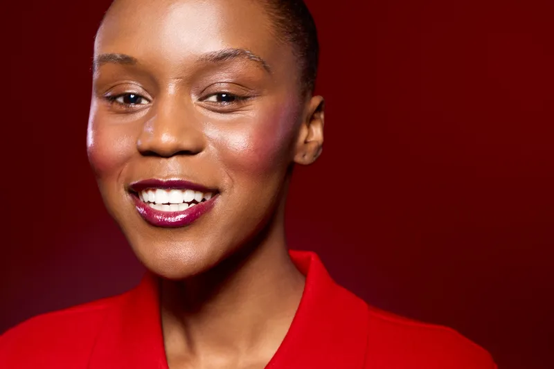 Happy African woman with dark skin smiling confidently in red clothing. Close-up portrait on red background. Concept of beauty, confidence, and positive emotions.