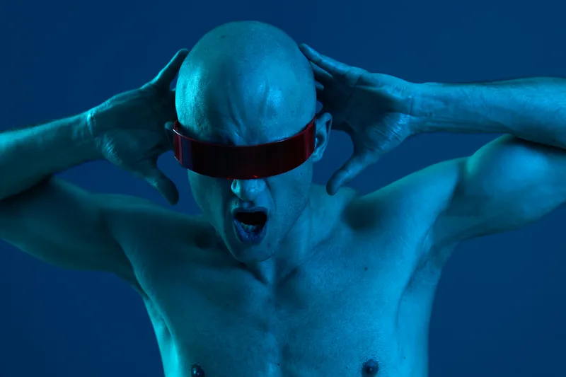 A distressed man with futuristic sunglasses expressing intense emotions in a cool blue light, showcasing the power of self-expression and modern style.