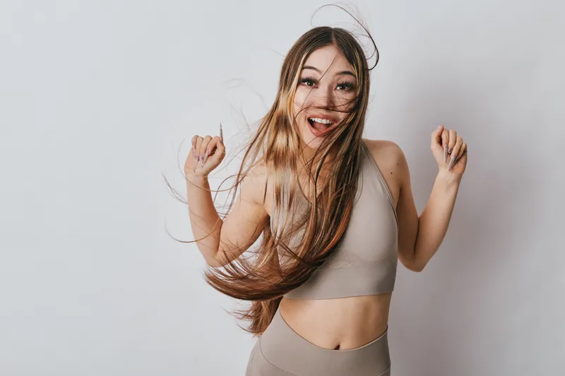 Happy young woman with long hair wearing sporty crop top and leggings smiling and dancing against white background for fitness and active lifestyle concept.