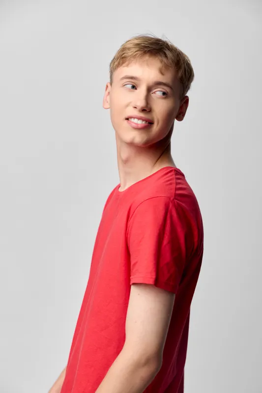 Youthful male in a red tshirt, side profile, casual fashion in a studio with bright lighting and clean background, conveying a relaxed mood and modern everyday style.