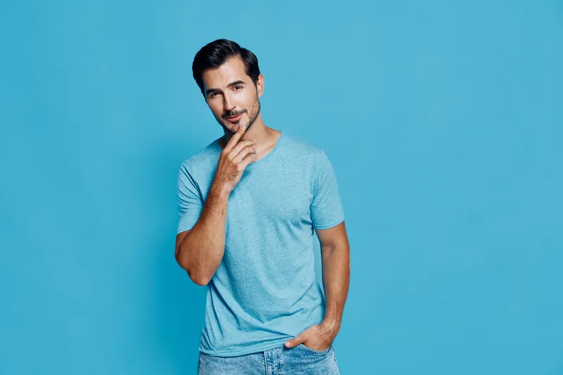 Charming smiling man in casual blue t-shirt posing against a vibrant blue background with a thoughtful expression, creating a relaxed and engaging vibe.
