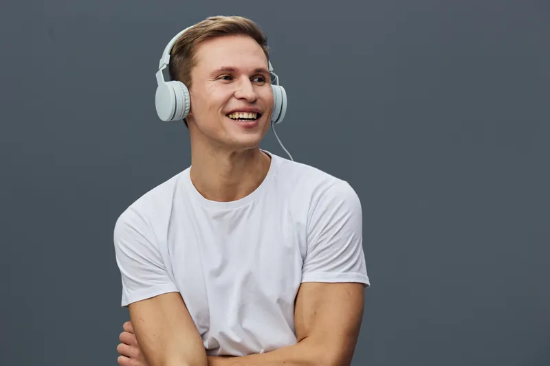 Smiling man wearing headphones and white t-shirt, looking happy and relaxed, isolated on plain gray background, studio portrait, casual style, positive emotion, leisure concept