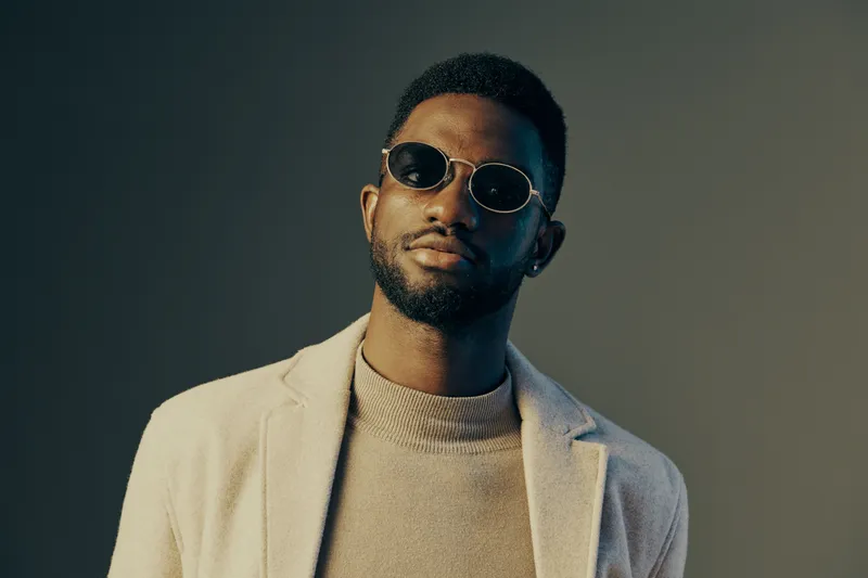 Stylish young Black man wearing sunglasses and a beige blazer, exuding confidence against a gradient background, perfect for fashion and lifestyle themes
