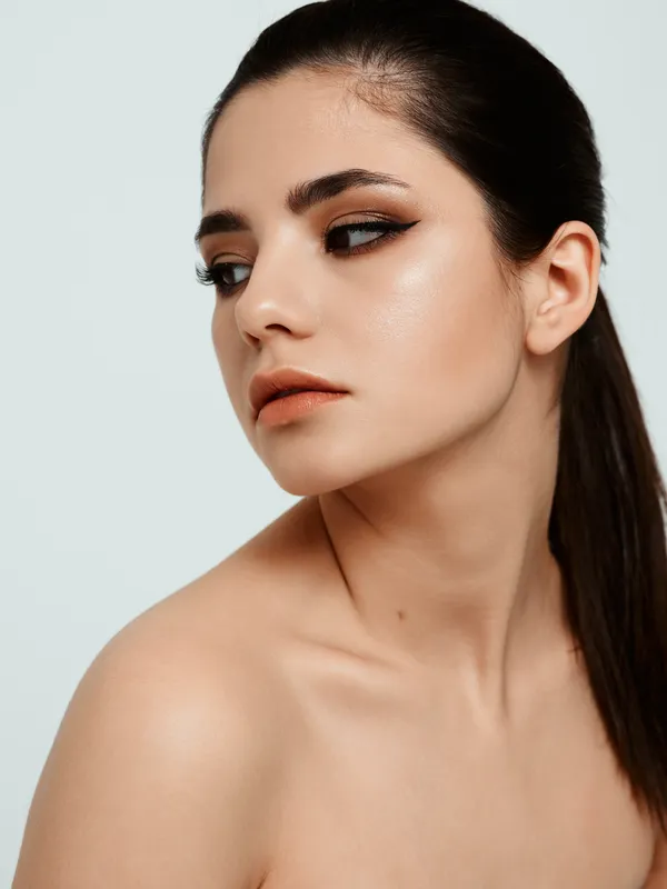 Привлекательная брюнетка с вечерним макияжем на лице, обнаженные плечи, светлый фон