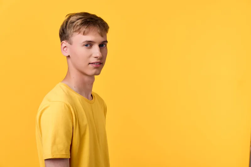 Man in yellow shirt stands against a solid yellow background, a bright studio fashion shot with clean lines, minimal setup, soft lighting, and a bold monochrome look that highlights casual style and