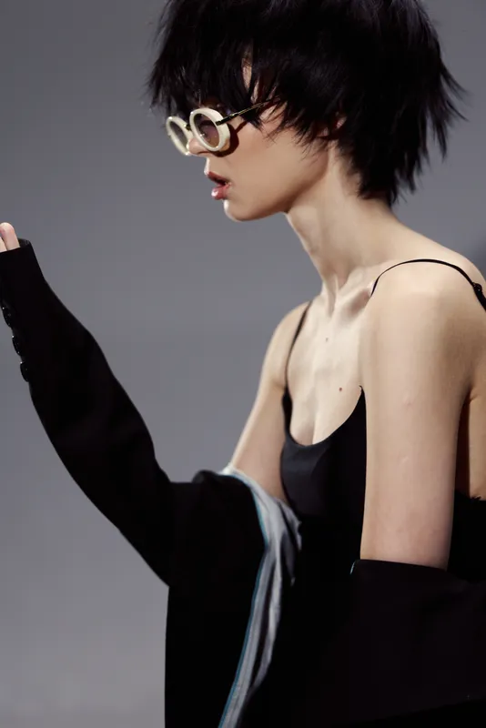 Young woman with short hair wearing stylish glasses and black clothing in a minimalist studio setting