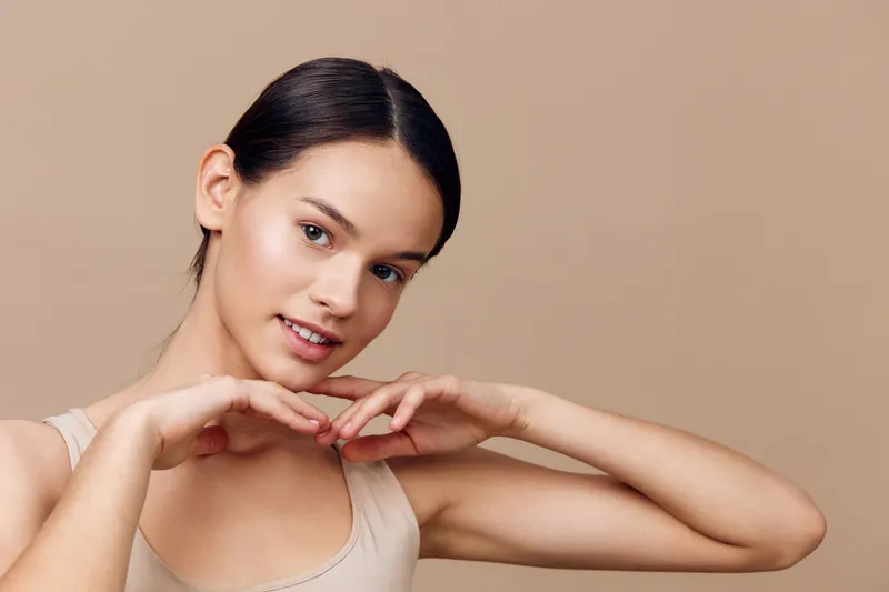 Smiling young model with a neutral background showcasing beauty and confidence, perfect for wellness, skincare, and fashion concepts