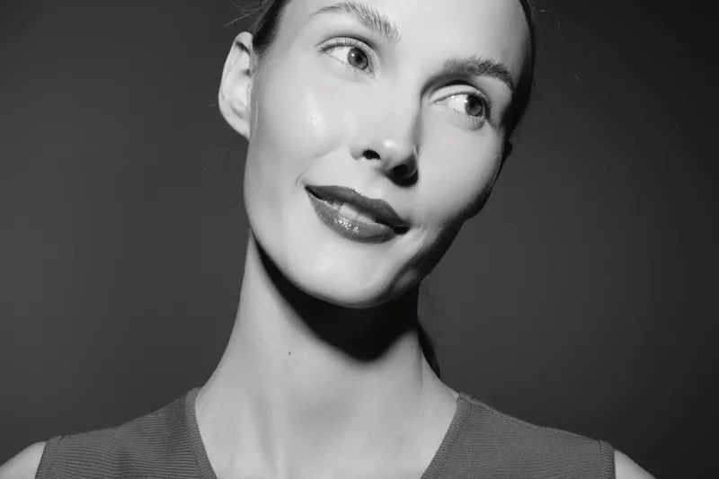 Closeup portrait of a young white woman with fair skin and dark hair looking aside. Monochrome image with soft lighting and neutral background.