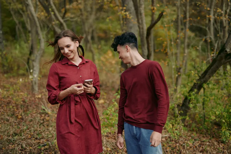 A candid portrait of a young couple sharing an authentic, genuine moment in a forest clearing, the woman smiling at her phone while the man looks on, captured with natural light and realistic