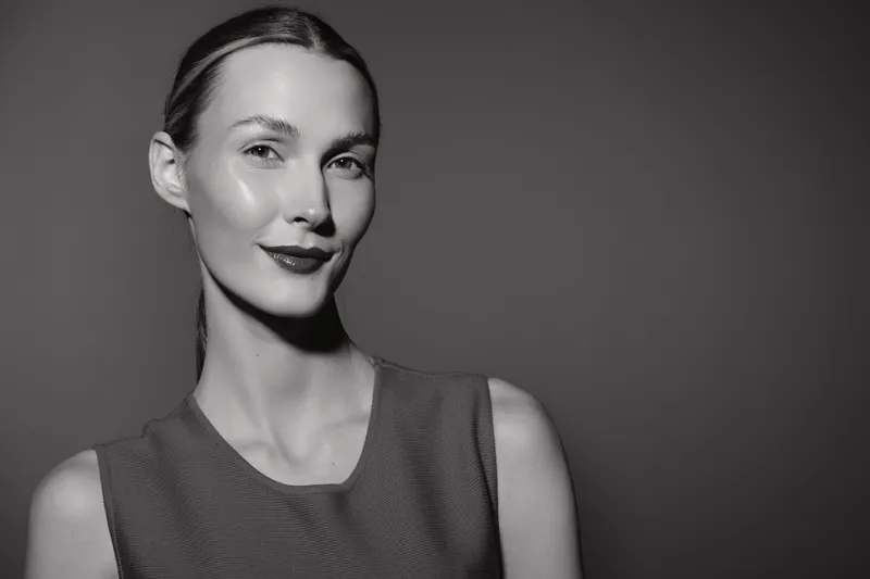 Portrait of a young Caucasian woman with fair skin and slicked back hair smiling confidently against a plain dark background. Concept of beauty and elegance.