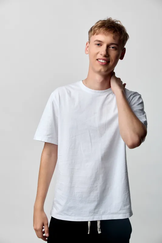 Young man in a white t shirt poses casually in a studio, light gray background, relaxed expression, natural stance, clean fashion scene, everyday wardrobe, simple contemporary style, minimal