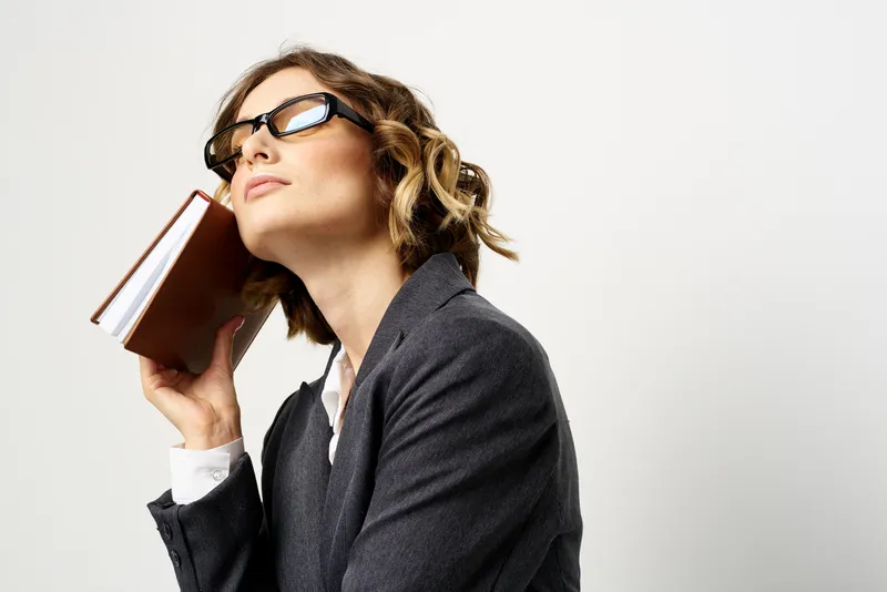Женщина на работе с книгой в руке на светлом фоне, в классическом костюме и очках, изображение головы